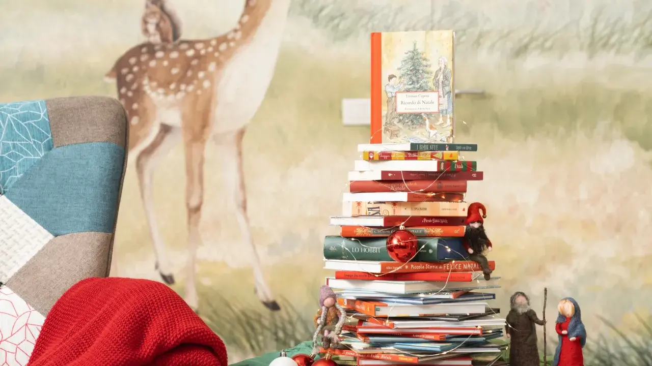Una pila di libri per le letture di Natale per bambini, decorata con lucine e palline rosse, con un folletto e statuine del presepe.