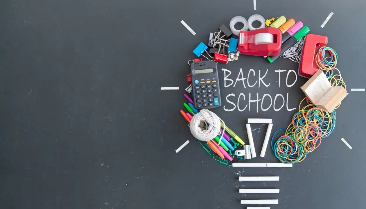 Un'idea luminosa per un buon inizio di anno scolastico: calcolatrice, penne, elastici e altri materiali scolastici formano una lampadina su lavagna.