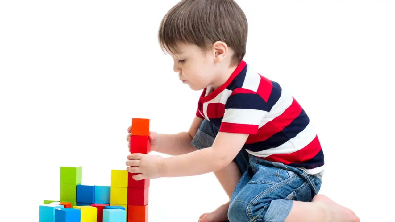 Bambino costruisce torre con blocchi colorati, esercitando la motricità fine. Obiettivi per lo sviluppo cognitivo e manuale.