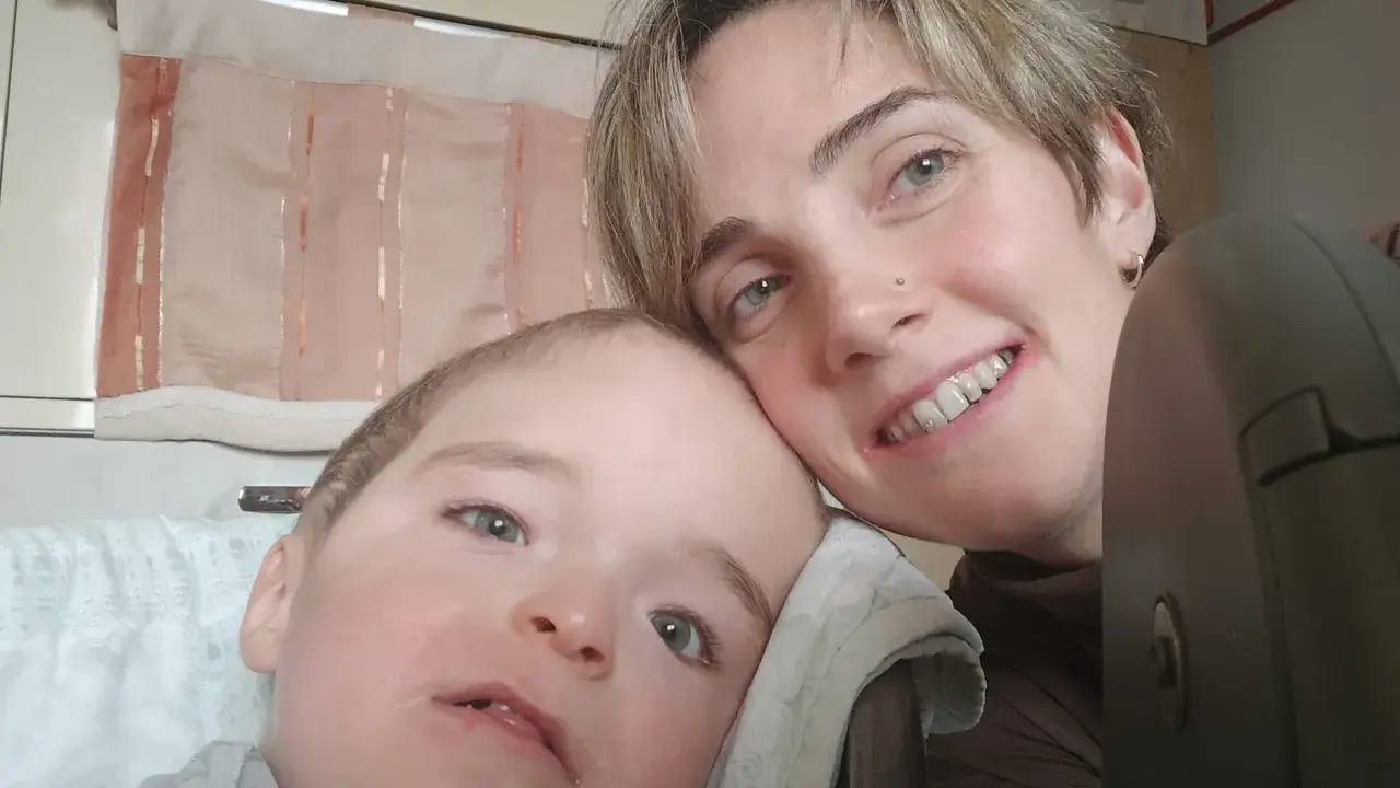 Un bambino con sindrome di down lieve e sua madre sorridono. La sua espressione dolce e i suoi occhi chiari sono un segno di amore.