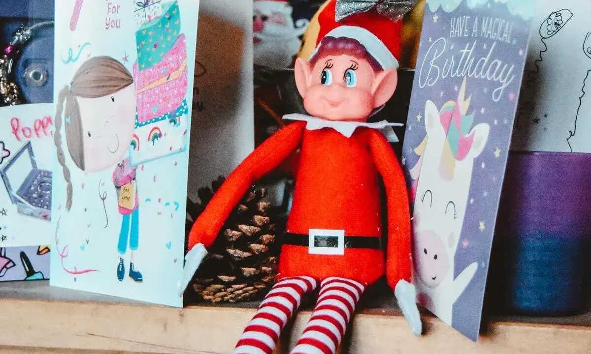 Un elfo di Natale, con il suo vestito rosso e calze a righe, è seduto tra biglietti d'auguri. La sua storia è legata alla magia delle feste e dei compleanni.