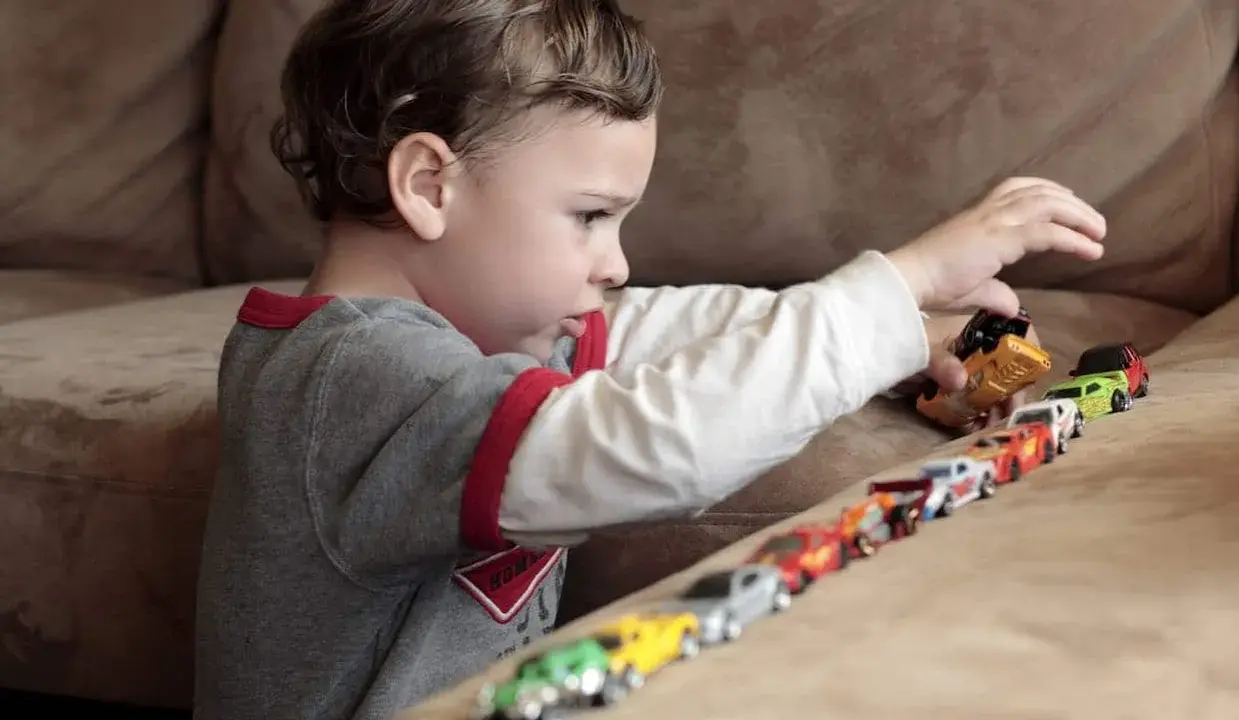 Bambino gioca con macchinine, creando una fila colorata. Le sue mani si muovono con un ritmo ipnotico, un esempio di stimming mani.