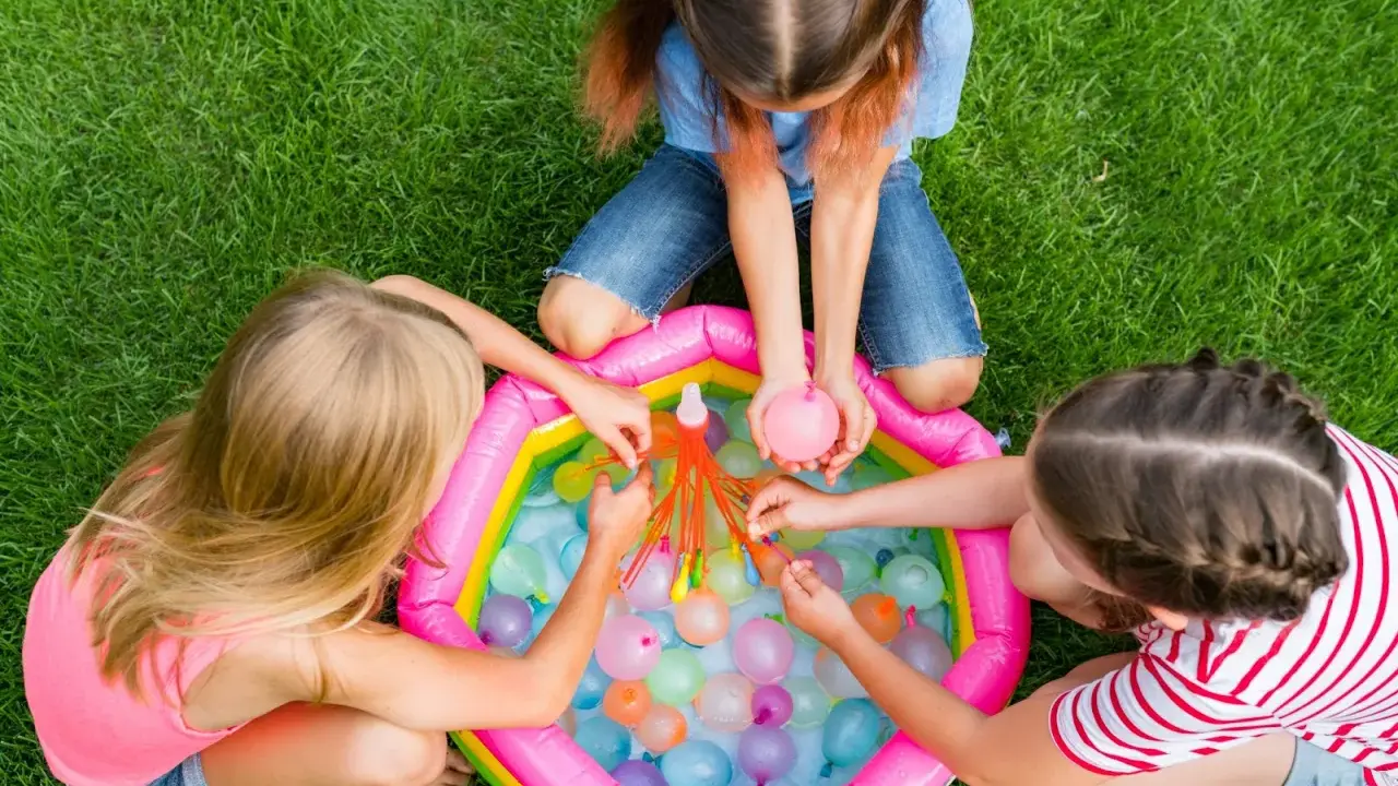 Bambini di 6 anni si divertono con giochi d'acqua in giardino, perfetti per un compleanno estivo.