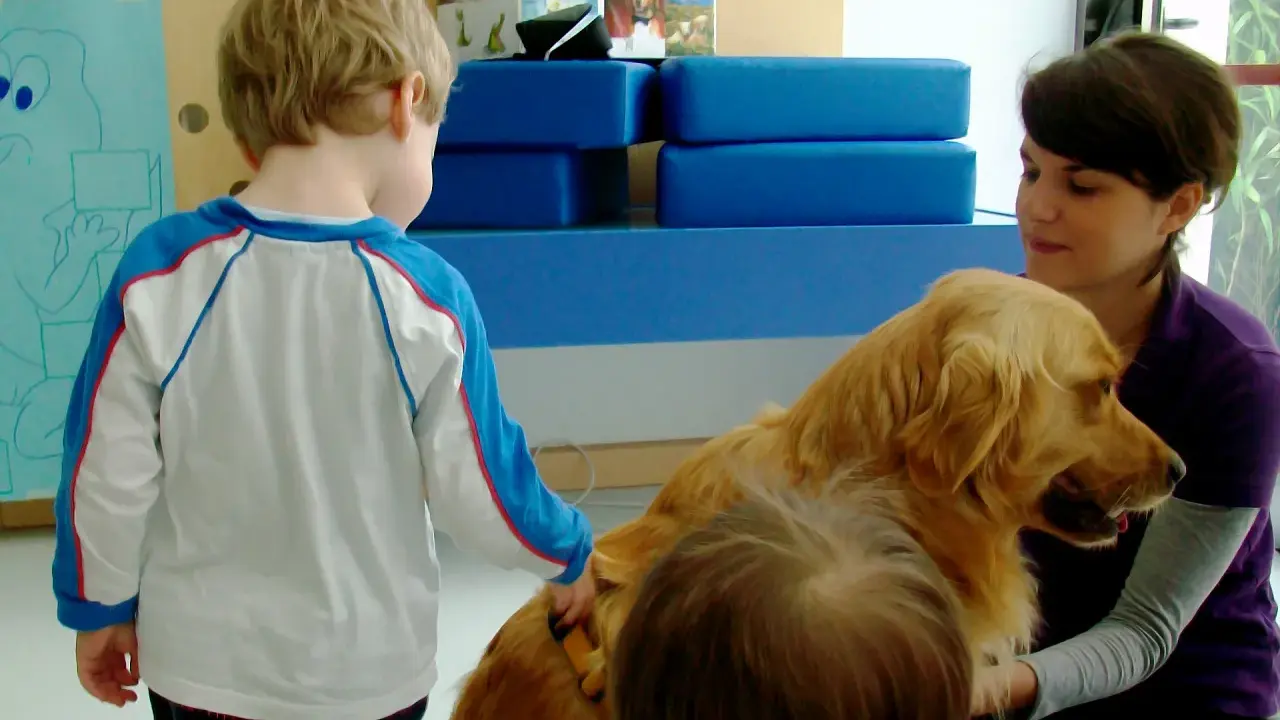 Un bambino interagisce con un cane durante una sessione di pet therapy. La donna sorride mentre il cane è accarezzato.