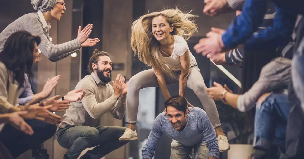 Un gruppo di amici si diverte con giochi da fare in gruppo seduti senza niente, una donna salta su un uomo mentre gli altri applaudono.