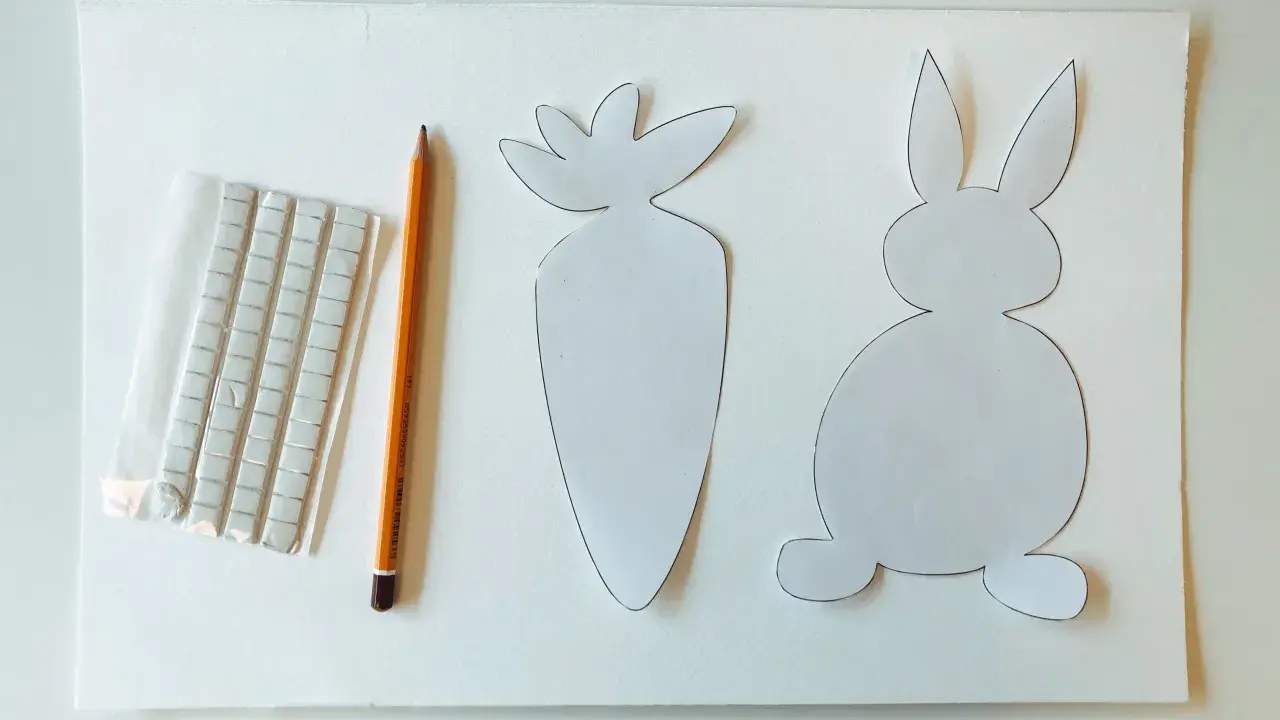 Sagoma di coniglietto e carota, matita e adesivi per creare decorazioni pasquali.