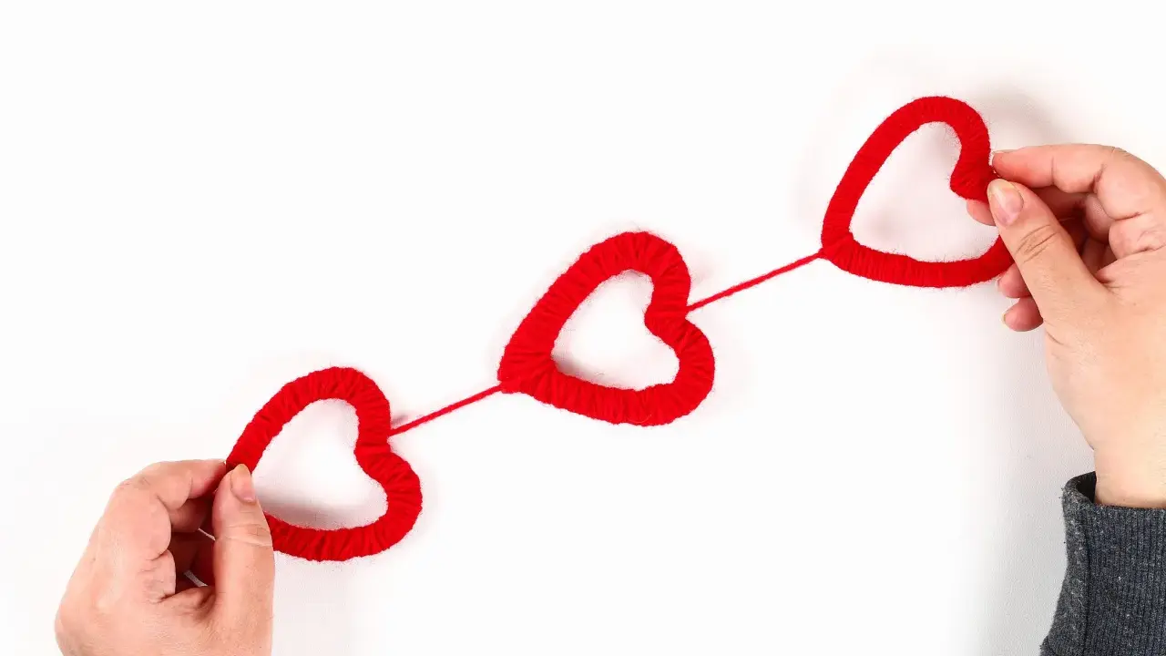 Mani che creano cuori rossi di lana, perfetti per lavoretti per San Valentino.