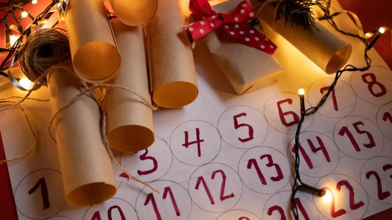 Un **calendario avvento fai da te cartoncino** con rotoli di carta marrone legati con spago, luci natalizie e un piccolo pacchetto regalo.