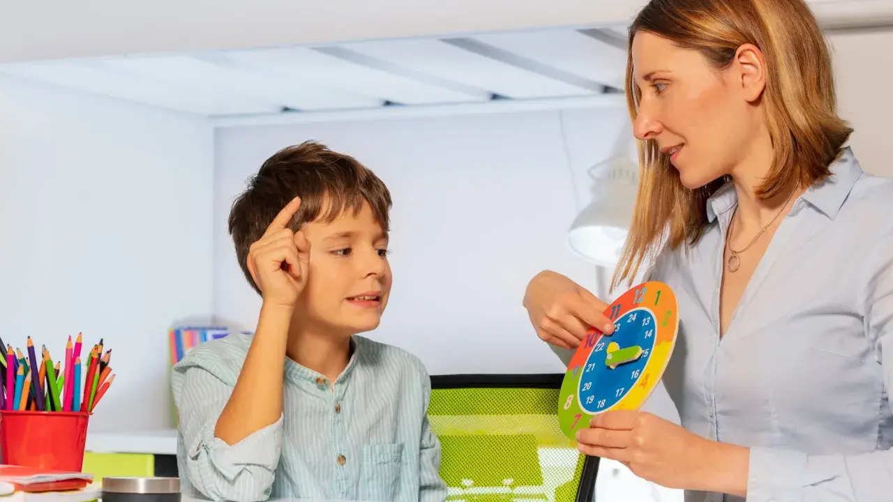 Bambino concentrato durante una sessione di terapia occupazionale, impara a leggere l'ora con un colorato orologio didattico.