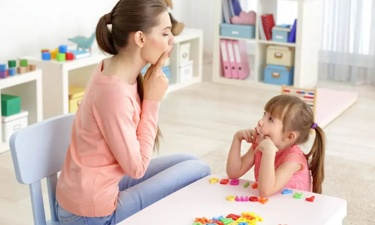 Logopedista e bambina fanno esercizi di logopedia con lettere colorate sul tavolo.