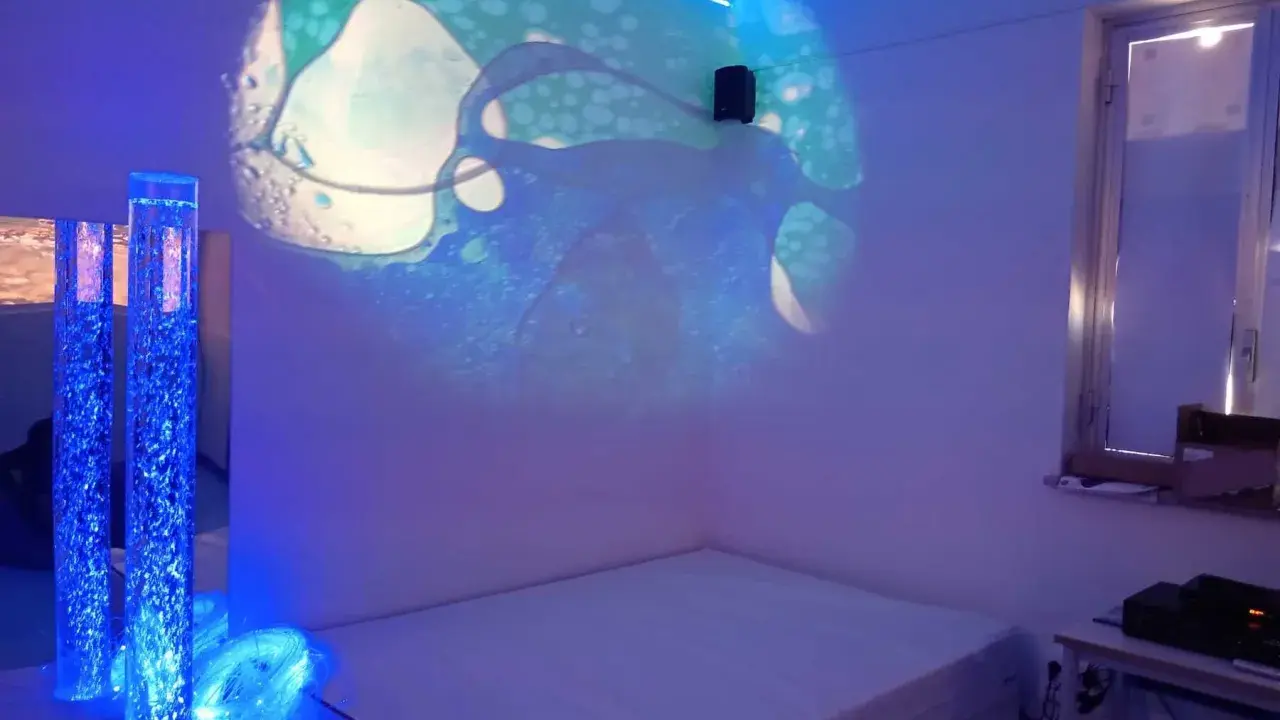 Un'aula snoezelen con proiezioni luminose, colonne d'acqua blu e un letto. Un ambiente rilassante e multisensoriale.