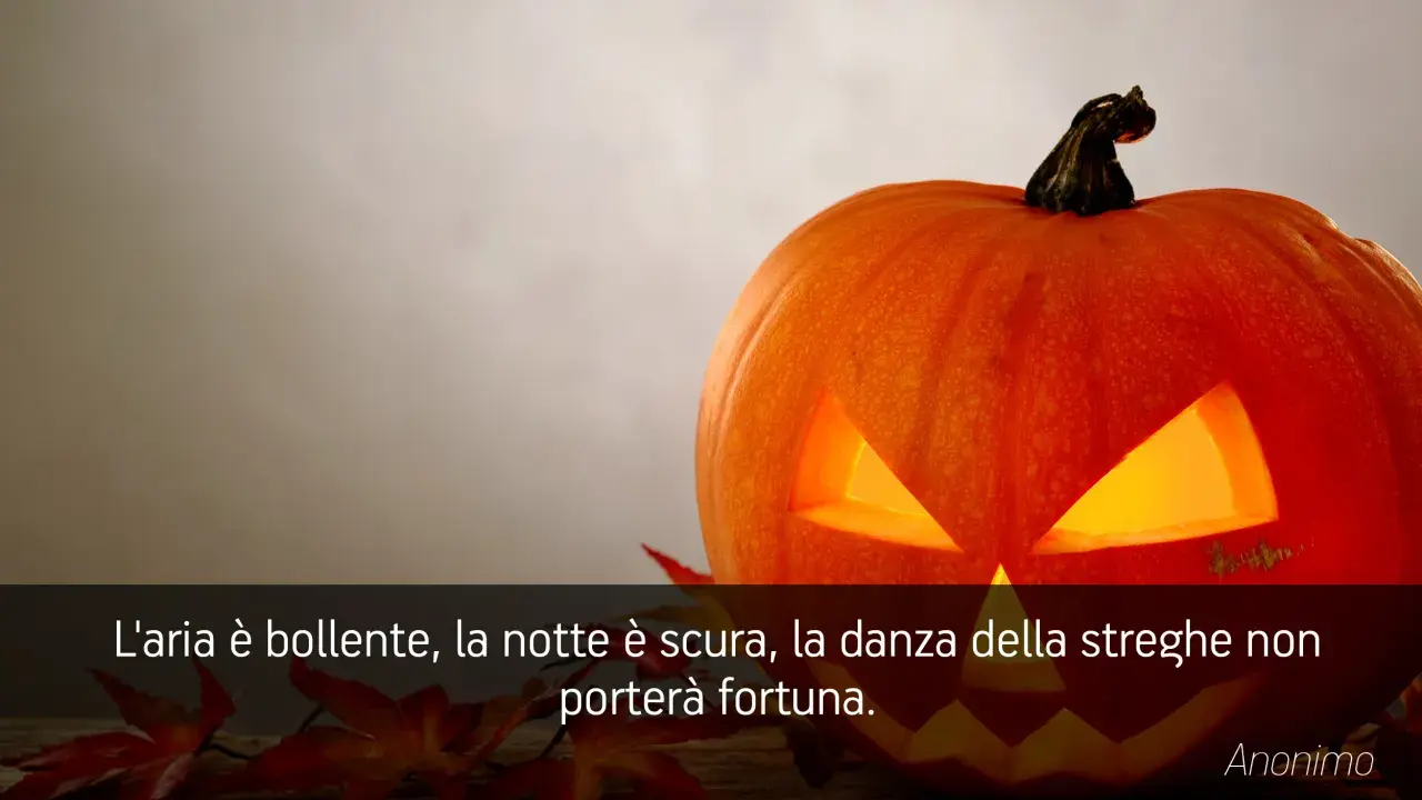 Zucca di Halloween illuminata, con foglie rosse e una citazione: "L'aria è bollente, la notte è scura, la danza della streghe non porterà fortuna." Perfetta per frasi di Halloween per bambini.