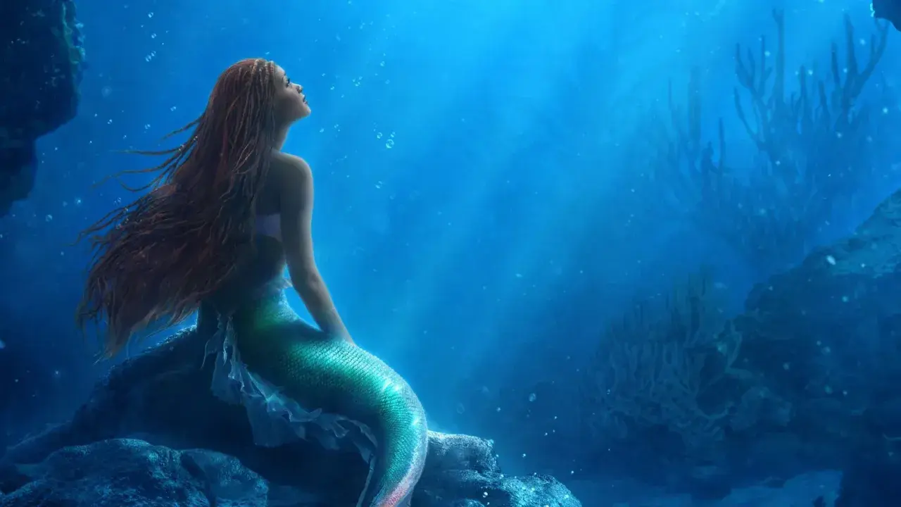 La sirenetta storia breve: una giovane sirena dai capelli rossi guarda verso l'alto, sognando il mondo di sopra, seduta su una roccia sottomarina.