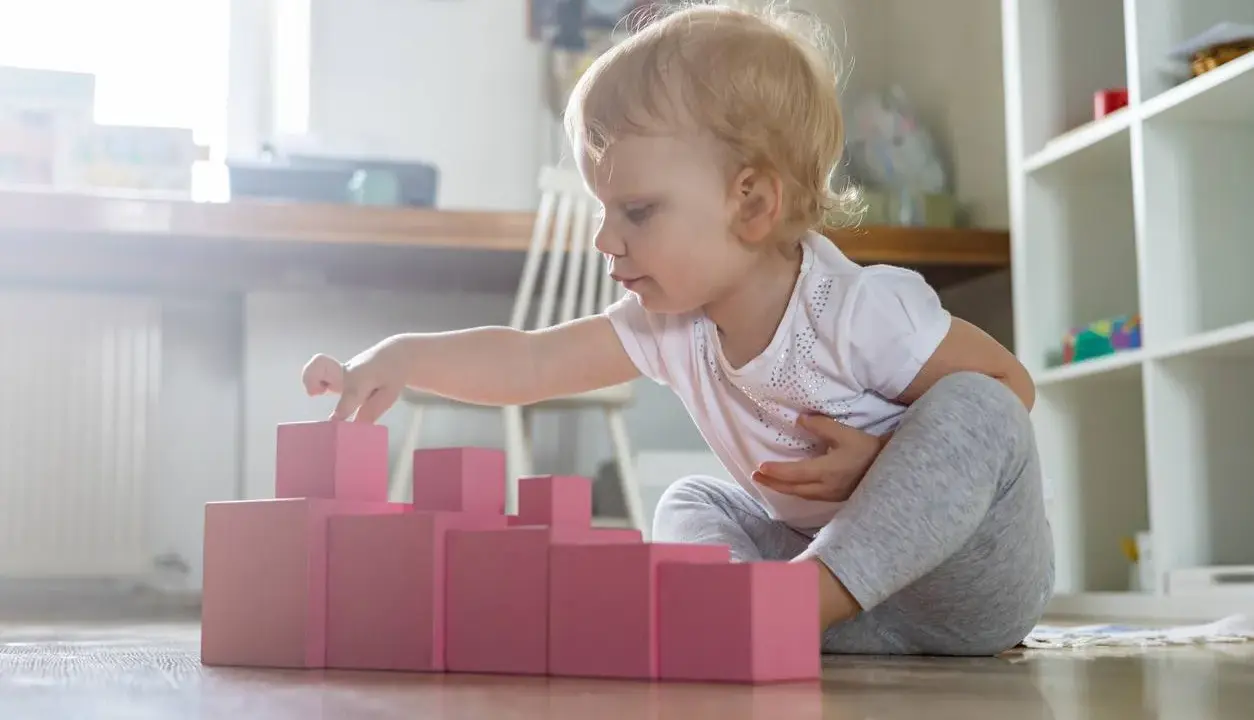 Bambina di 1 anno gioca con blocchi rosa, un'attività divertente in casa per sviluppare la coordinazione.