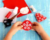 Bambino crea decorazioni natalizie in feltro. Materiali per attività natalizie per bambini: forbici, filo rosso e bianco, feltro rosso e bianco.