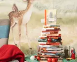 Una pila di libri per le letture di Natale per bambini, decorata con lucine e palline rosse, con un folletto e statuine del presepe.