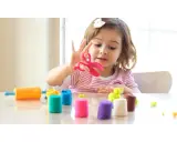 Bambina gioca con pasta modellabile colorata, forbici rosa e mattarello arancione. Giochi di manipolazione Montessori per sviluppare creatività.