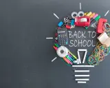 Un'idea luminosa per un buon inizio di anno scolastico: calcolatrice, penne, elastici e altri materiali scolastici formano una lampadina su lavagna.