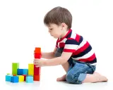 Bambino costruisce torre con blocchi colorati, esercitando la motricità fine. Obiettivi per lo sviluppo cognitivo e manuale.
