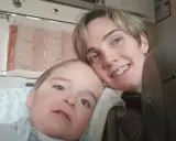 Un bambino con sindrome di down lieve e sua madre sorridono. La sua espressione dolce e i suoi occhi chiari sono un segno di amore.