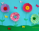 Lavoretti primavera: fiori colorati con bottoni e farfalle di carta su sfondo azzurro.