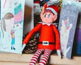 Un elfo di Natale, con il suo vestito rosso e calze a righe, è seduto tra biglietti d'auguri. La sua storia è legata alla magia delle feste e dei compleanni.
