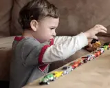 Bambino gioca con macchinine, creando una fila colorata. Le sue mani si muovono con un ritmo ipnotico, un esempio di stimming mani.