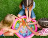 Bambini di 6 anni si divertono con giochi d'acqua in giardino, perfetti per un compleanno estivo.