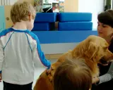Un bambino interagisce con un cane durante una sessione di pet therapy. La donna sorride mentre il cane è accarezzato.