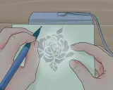 Mani che creano un disegno floreale con uno strumento su carta illuminata, un'arte di embossing su carta.