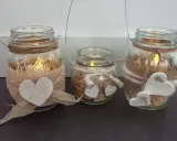 Tre vasetti lanterne fai da te decorati con cuori e spago, con candele accese all'interno per un'atmosfera calda.