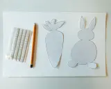 Sagoma di coniglietto e carota, matita e adesivi per creare decorazioni pasquali.