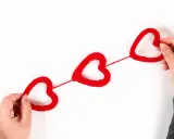 Mani che creano cuori rossi di lana, perfetti per lavoretti per San Valentino.