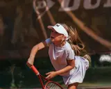 Bambina concentrata durante un servizio di tennis, con la racchetta pronta a colpire la palla.