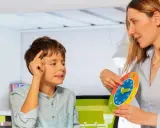 Bambino concentrato durante una sessione di terapia occupazionale, impara a leggere l'ora con un colorato orologio didattico.