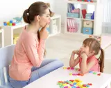 Logopedista e bambina fanno esercizi di logopedia con lettere colorate sul tavolo.