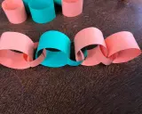 Una catena di carta colorata, con anelli arancioni e verdi intrecciati, pronta per decorare.
