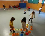 Bambini si divertono con giochi psicomotricità 3 anni: corrono, saltano ostacoli e camminano su coni colorati in palestra.