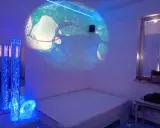 Un'aula snoezelen con proiezioni luminose, colonne d'acqua blu e un letto. Un ambiente rilassante e multisensoriale.