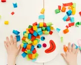 Bambini creano un clown con carta colorata, un'idea per lavoretti di Carnevale. Mani piccole e forbici rosa completano la scena.