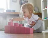Bambina di 1 anno gioca con blocchi rosa, un'attività divertente in casa per sviluppare la coordinazione.