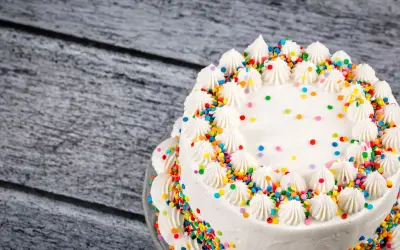 Torta compleanno bianca con glassa, decorata con ciuffi di panna e confettini colorati.