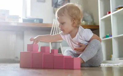 Bambina di 1 anno gioca con blocchi rosa, un'attività divertente in casa per sviluppare la coordinazione.