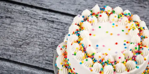 Torta compleanno bianca con glassa, decorata con ciuffi di panna e confettini colorati.