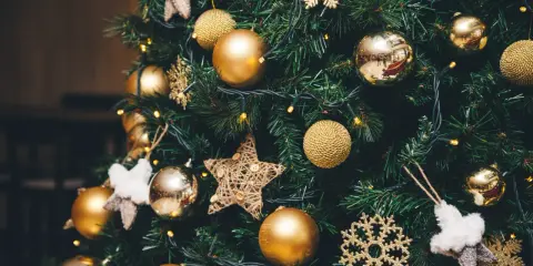 Un albero di Natale addobbato con palline dorate, fiocchi di neve scintillanti e stelle di stoffa. Le luci gialle creano un'atmosfera magica, un vero simbolo albero di natale.