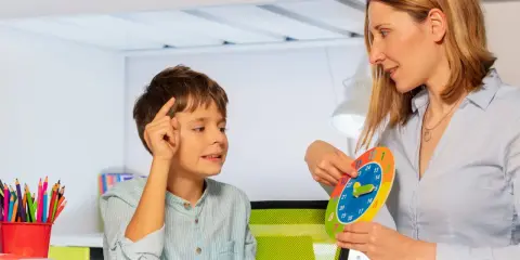 Bambino concentrato durante una sessione di terapia occupazionale, impara a leggere l'ora con un colorato orologio didattico.