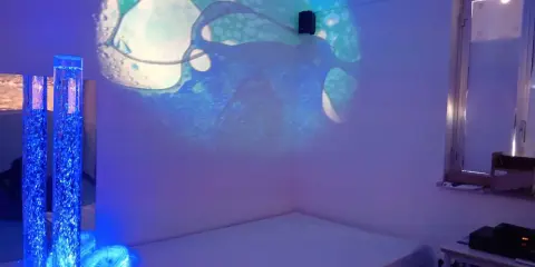 Un'aula snoezelen con proiezioni luminose, colonne d'acqua blu e un letto. Un ambiente rilassante e multisensoriale.