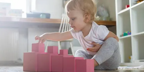 Bambina di 1 anno gioca con blocchi rosa, un'attività divertente in casa per sviluppare la coordinazione.
