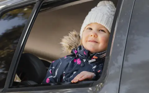 Bambina con cappellino bianco guarda fuori dal finestrino, pronta per i giochi da fare in macchina bambini.