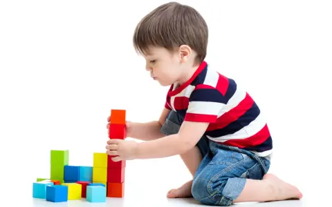 Bambino costruisce torre con blocchi colorati, esercitando la motricità fine. Obiettivi per lo sviluppo cognitivo e manuale.